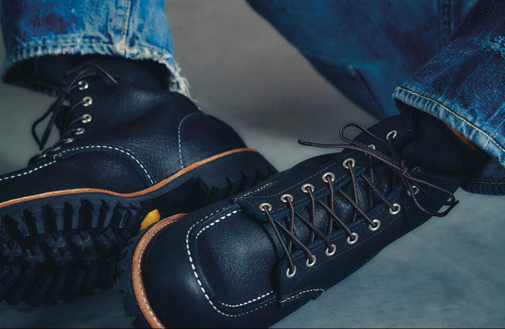 Navy blue boots with orange accents worn with blue jeans on a gray surface