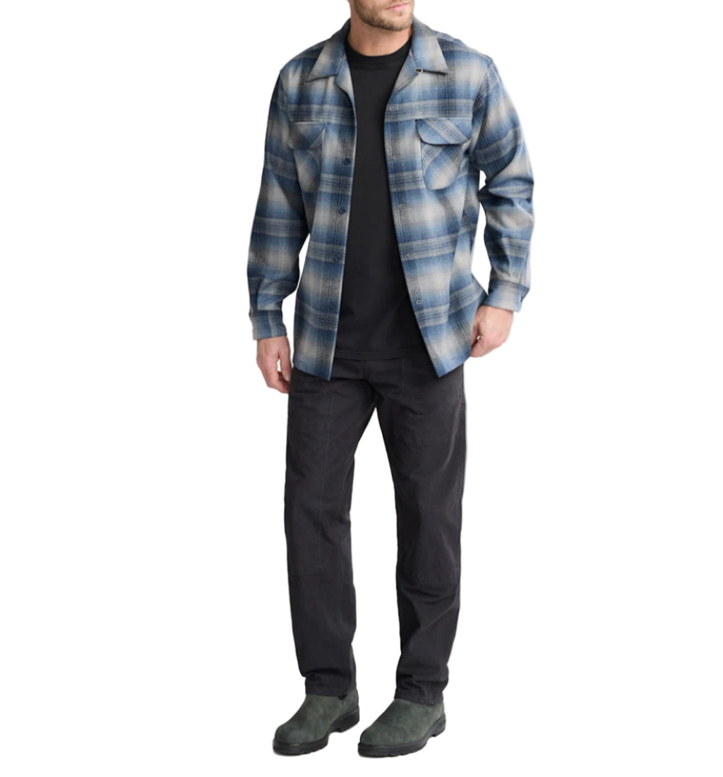 Man wearing a blue plaid shirt over a black t-shirt with dark pants on a white background