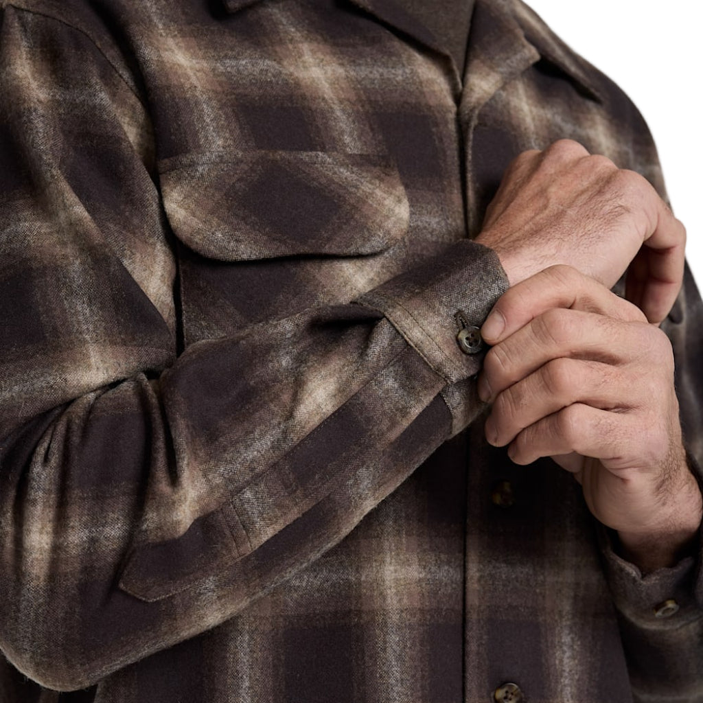 Close-up of a person wearing a brown plaid shirt with hands clasped together.