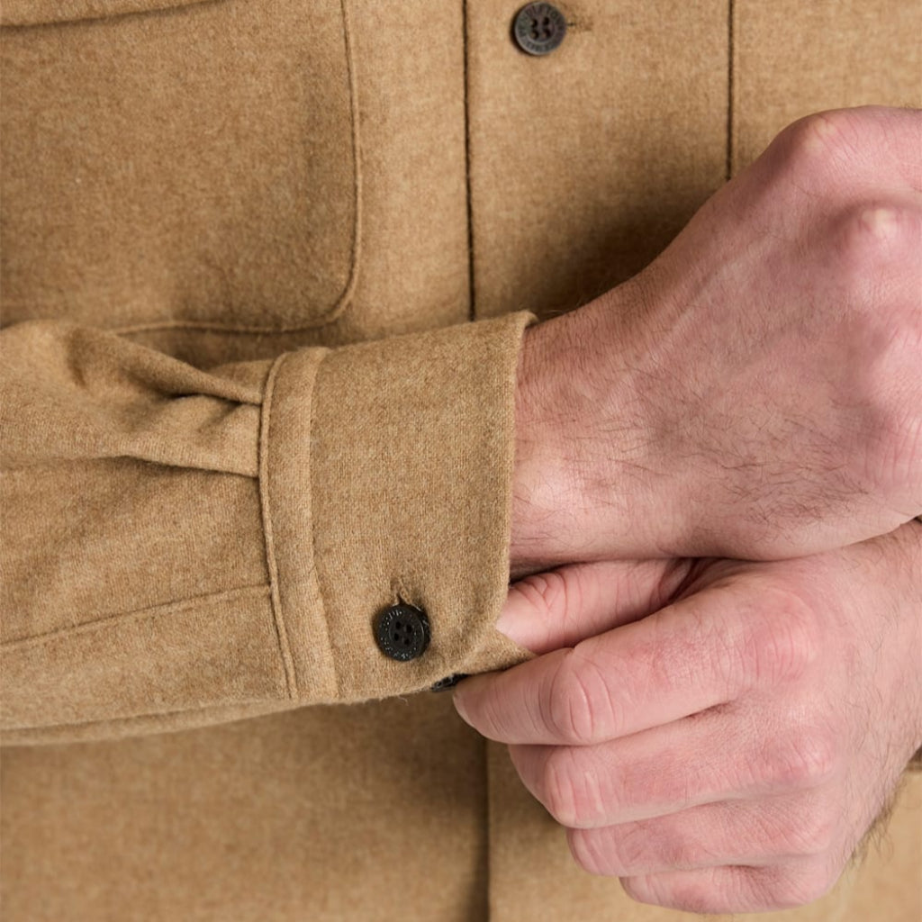 Close-up of a person wearing a beige shirt with button details, focusing on the sleeve and hands.