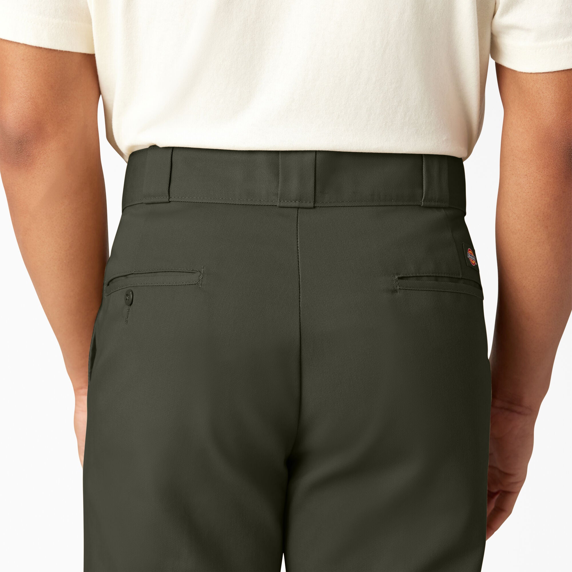 Person wearing dark green pants and a white shirt on a plain background