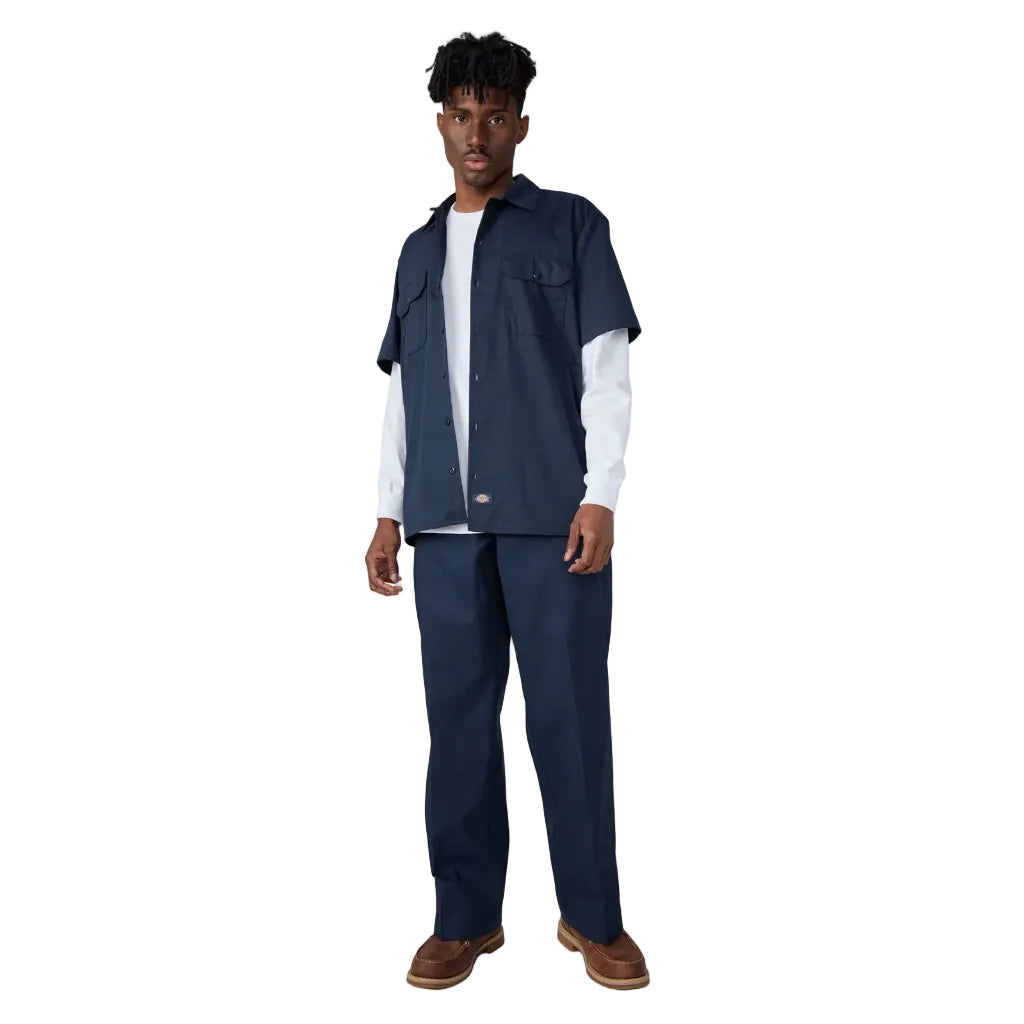 Person wearing a navy work shirt, pants, and vest on a white background