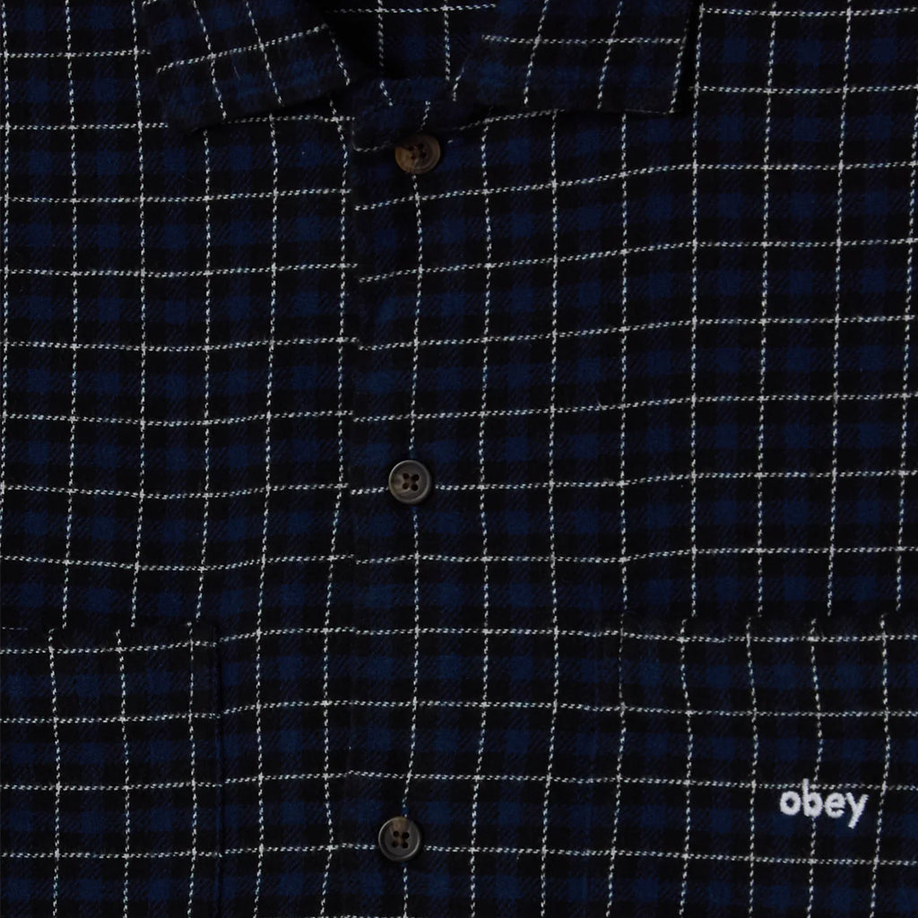 Close-up of a blue checkered shirt with 'obey' logo