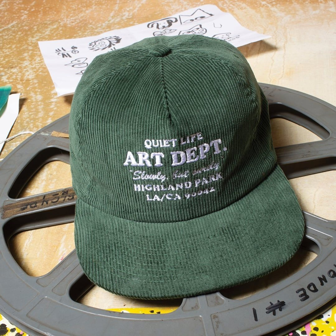 Green cap with 'Quiet Life Art Dept.' text on a film reel