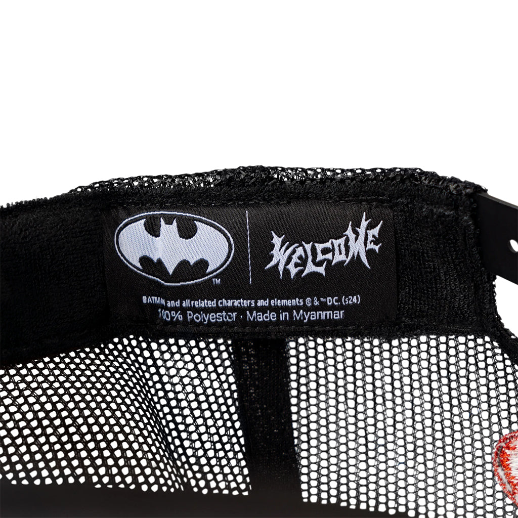 Close-up of a Batman logo on a label with 'Welcome' branding, on a black and white textured background.