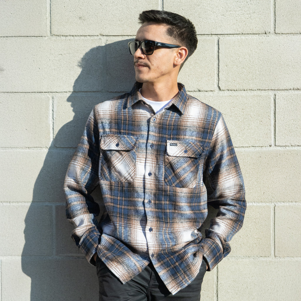 Man wearing a plaid shirt and sunglasses against a light gray brick wall
