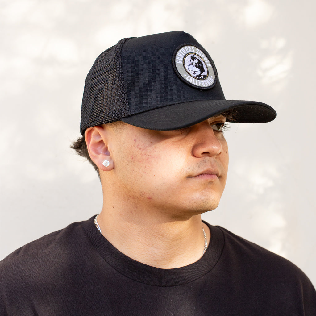 Person wearing a black cap with a logo on a light gray background