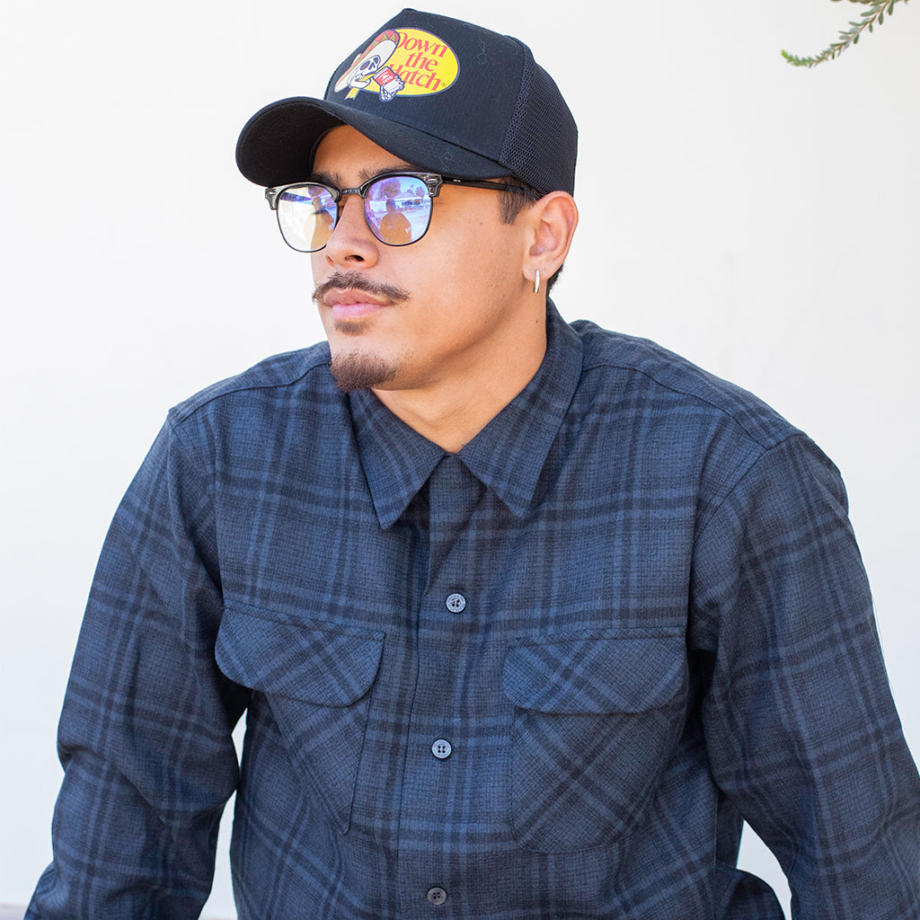 Man wearing a plaid shirt and cap with a visible brand logo against a white background
