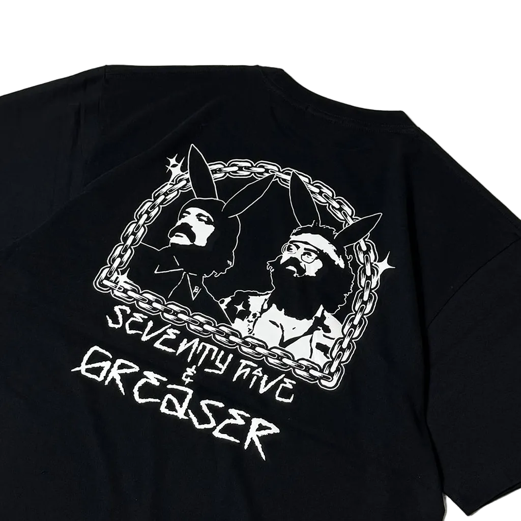 A close-up of a black short-sleeve T-shirt showing the back graphic. The design features a white chain-link border enclosing stylized portraits of two bearded men with bunny ears, with the text 'SEVENTY NINE & GREASER' printed below in a distressed white font.