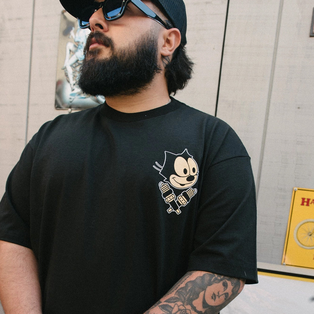 Man wearing a black t-shirt with a graphic design, standing against a light-colored wall.