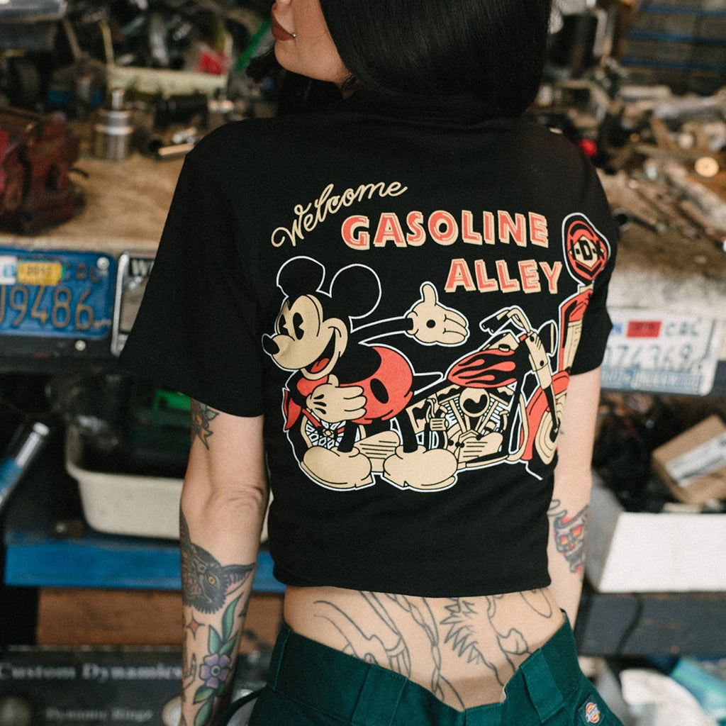 Person wearing a black t-shirt with a graphic design featuring Mickey Mouse and text 'Welcome to Gasoline Alley' in a workshop setting.