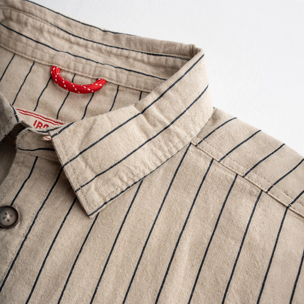 Close-up of a beige shirt with black pinstripes and a red tag on a white background