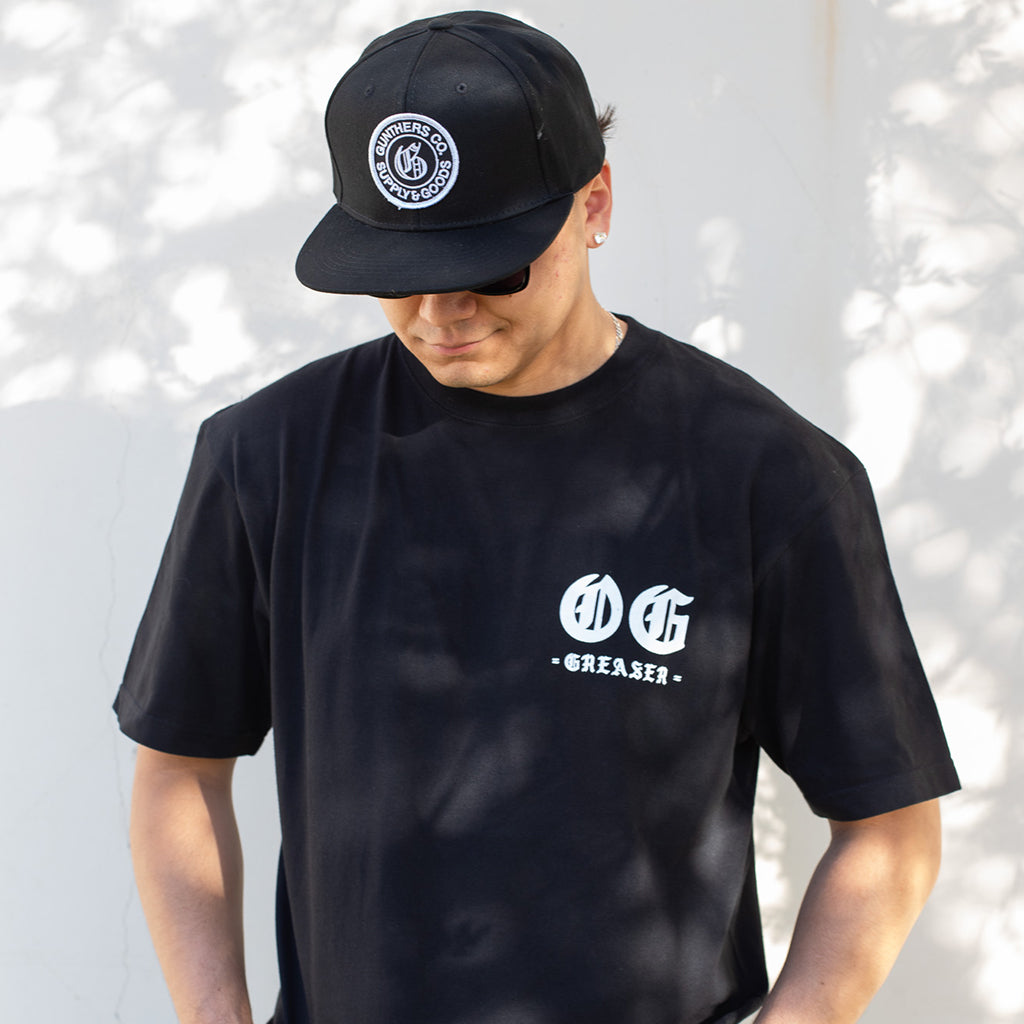 Person wearing a black t-shirt and cap with logos against a light background