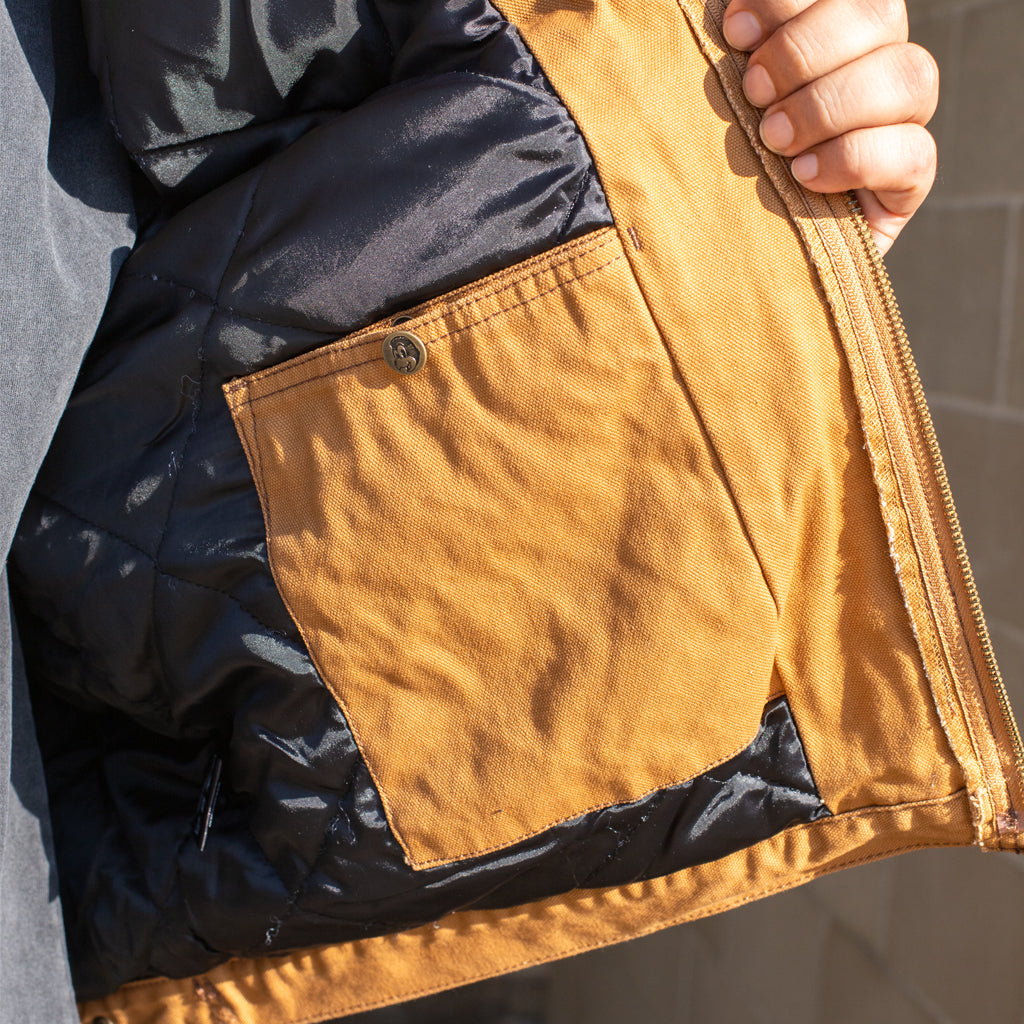 Close-up of a jacket with black and brown fabric, held by a hand.