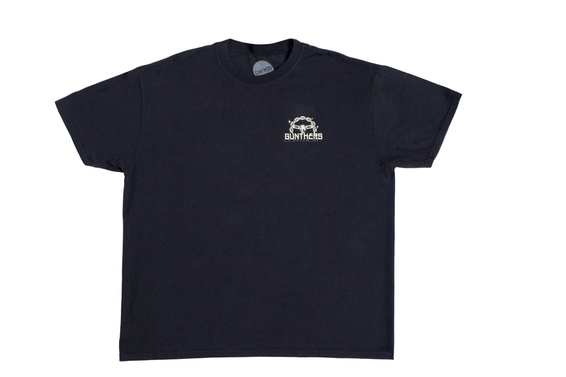 A black short-sleeve t-shirt with a small white chest graphic reading 'Gunthers' and a chain steering wheel, laid flat on a white surface next to a wood floor.