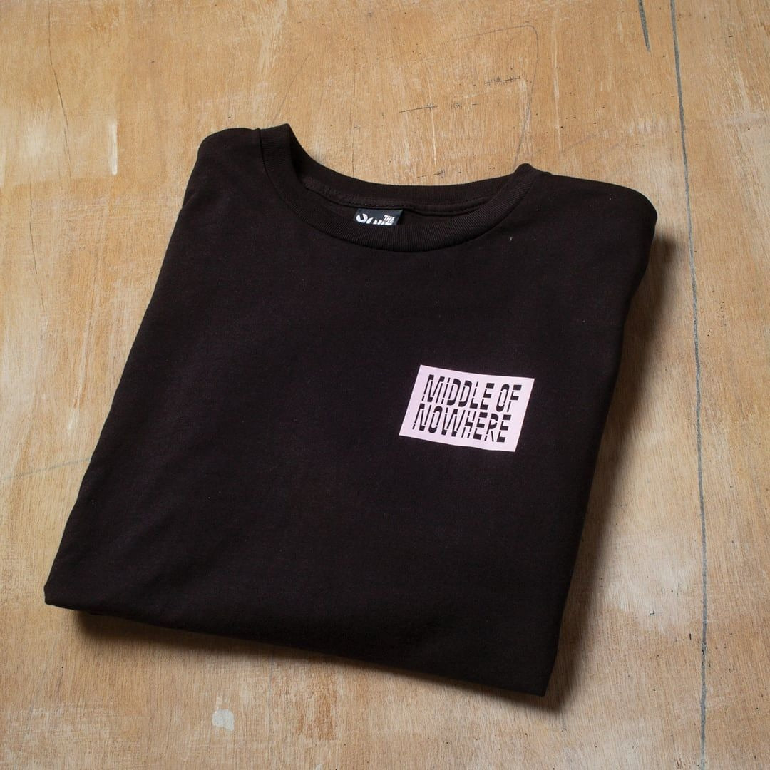 Folded black t-shirt with 'Middle of Nowhere' logo on a wooden surface