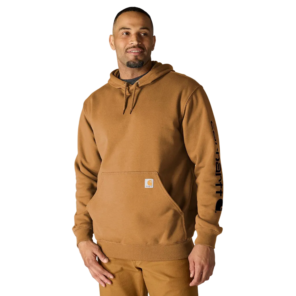 A man wearing a tan Carhartt pullover hoodie with black sleeve graphics and a small Carhartt logo patch on the front pocket, photographed against a plain white background.