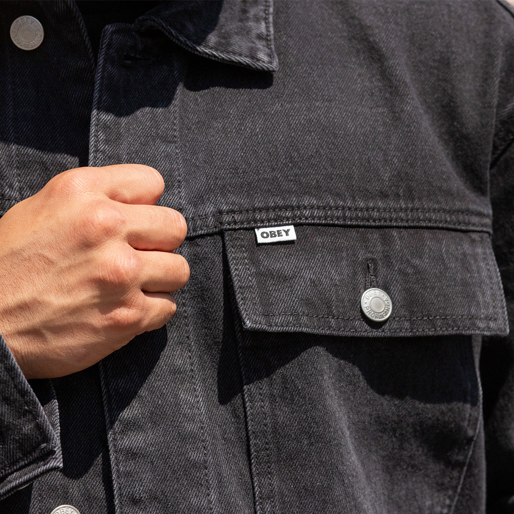 Close-up of a person wearing a dark denim jacket with a visible brand label.