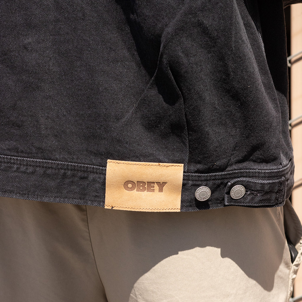 Close-up of a black jacket with an 'Obey' label on a blurred natural background
