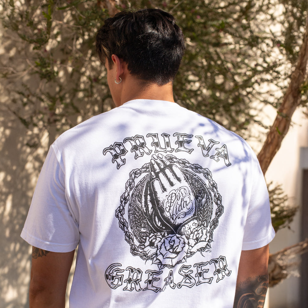 Person wearing a white t-shirt with black graphics and text outdoors