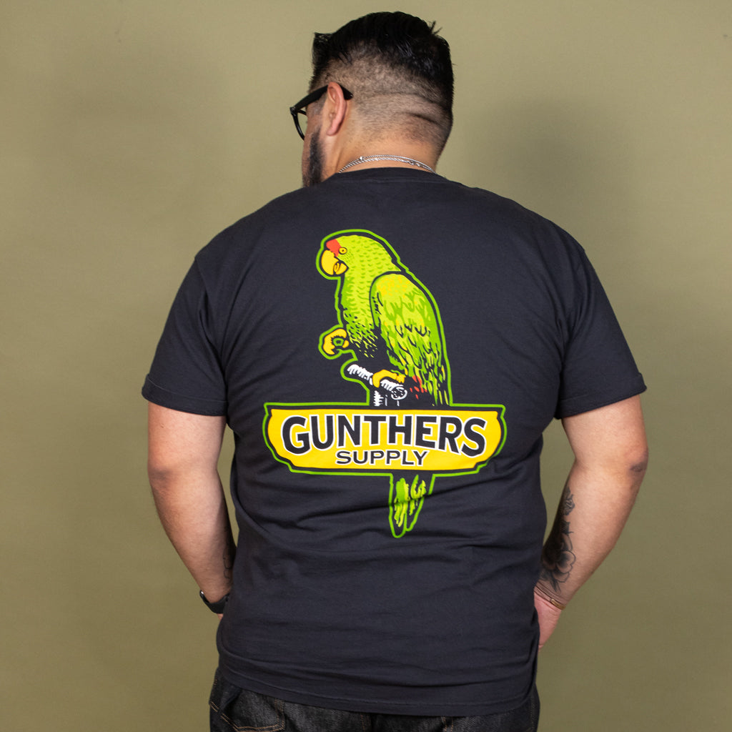 Person wearing a black t-shirt with a green parrot graphic and 'Gunthers Supply' text on the back.