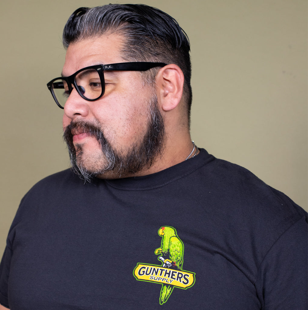 Man wearing a black t-shirt with a green parrot graphic and 'Gunther's Supply' text.