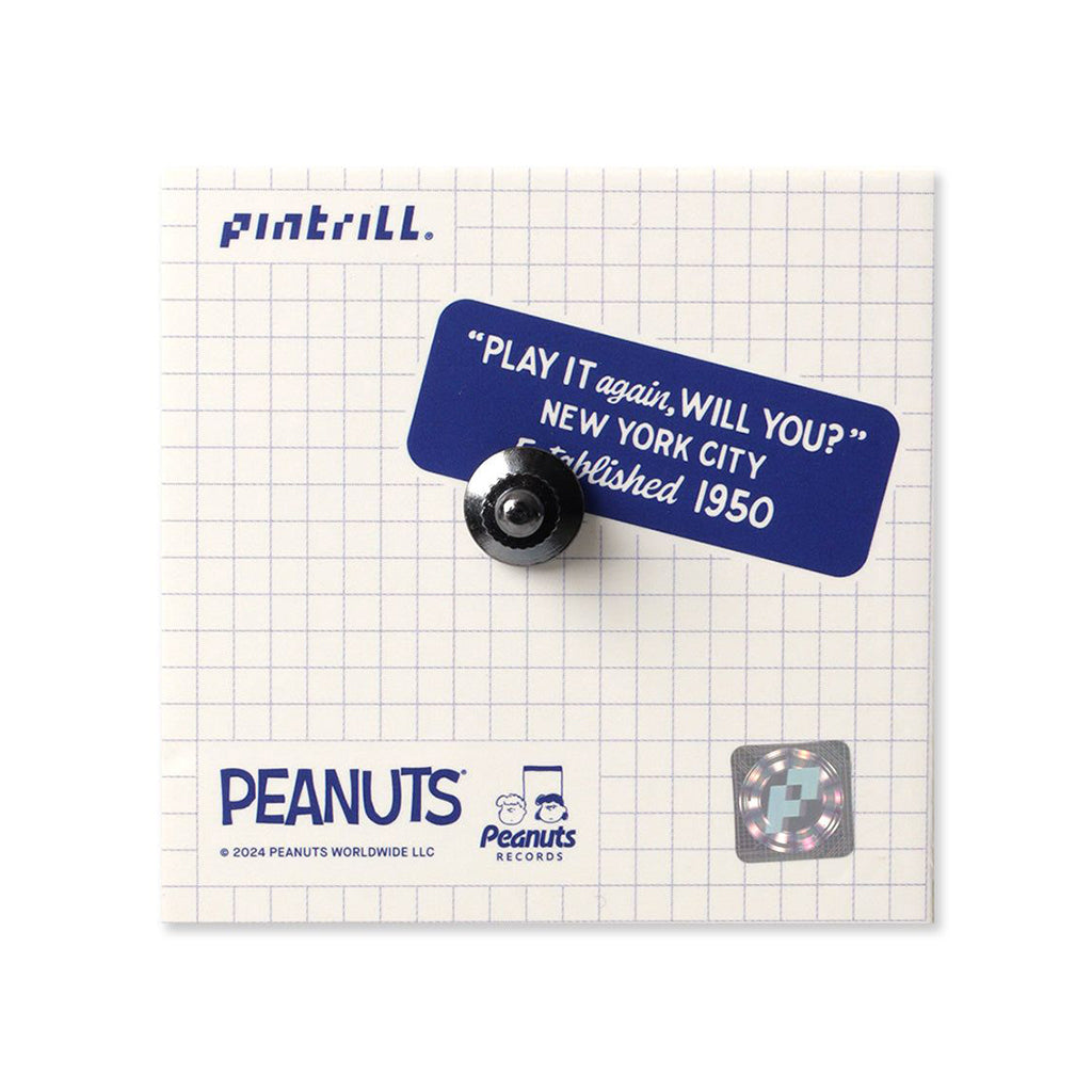 Pin with blue label and black pin backing on a grid background, featuring Peanuts branding.