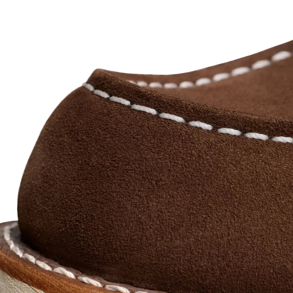 Close-up of a brown suede shoe with white stitching on a white background