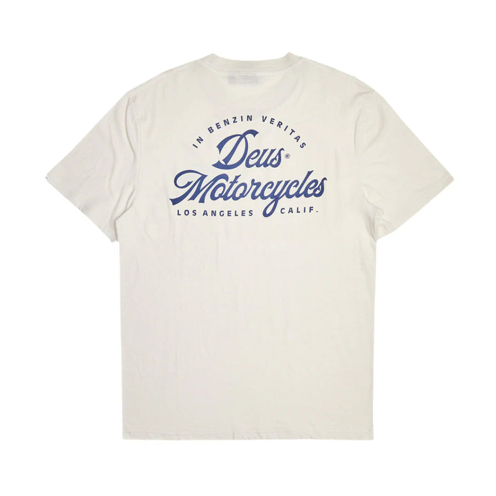 An off-white short-sleeve t-shirt with a blue graphic print on the front reading 'Deus Motorcycles' and 'In Benzin Veritas Los Angeles, Calif.' on a solid white background.
