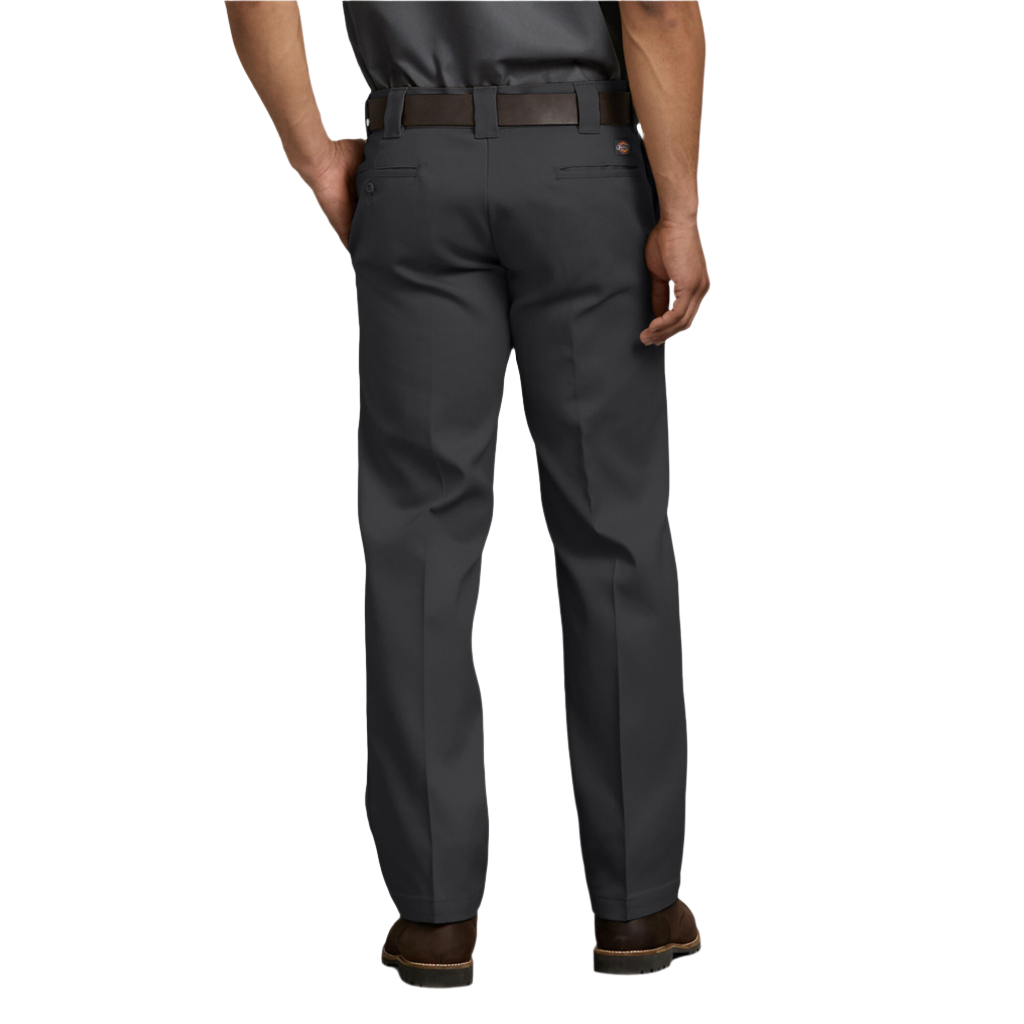 A man standing with hands in pockets wearing black Dickies men's 873 flex slim fit work pants and brown shoes.