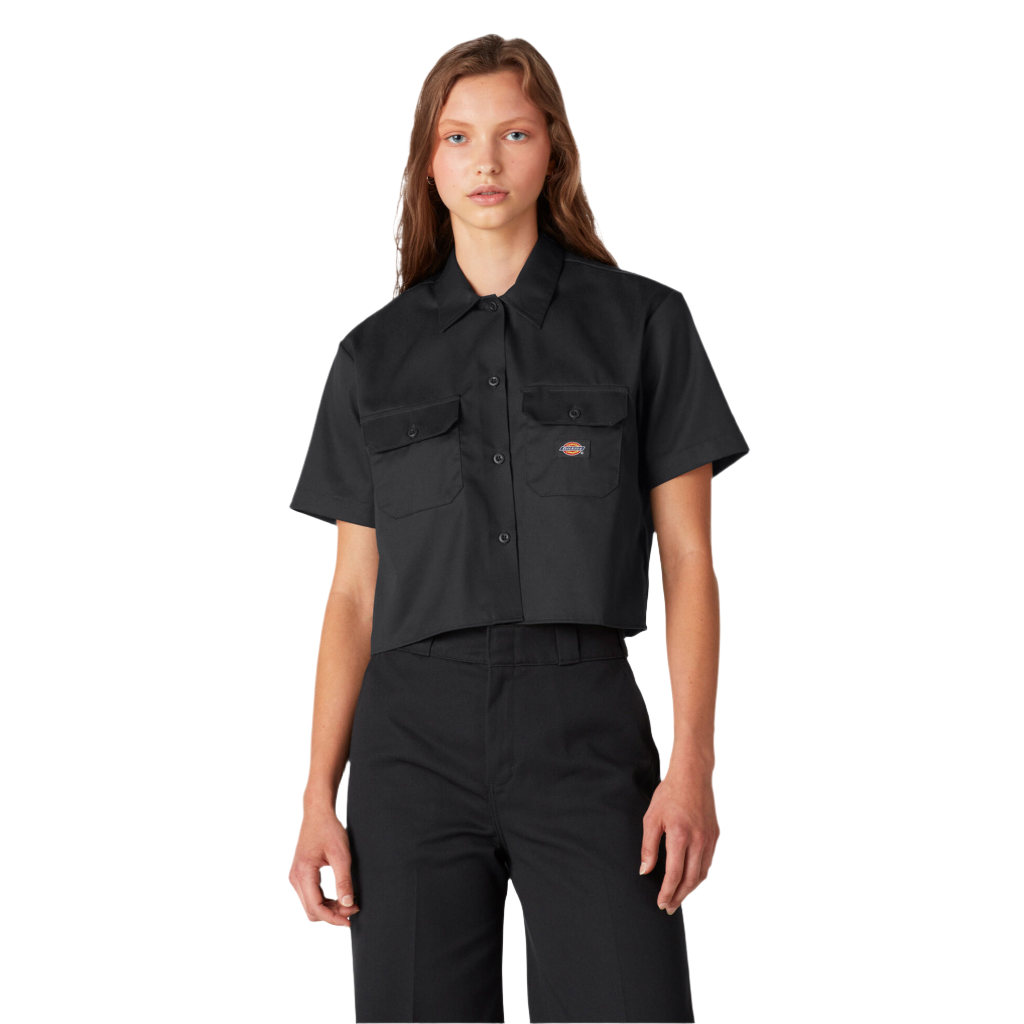 A woman wearing a black Dickies brand cropped work shirt with two flap chest pockets and a boxy silhouette.