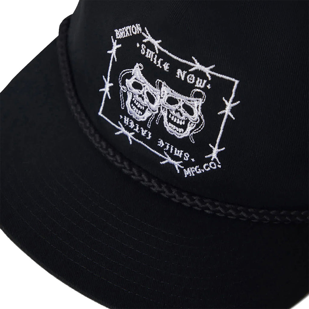 Black cap with white embroidered design featuring skulls and text on a white background
