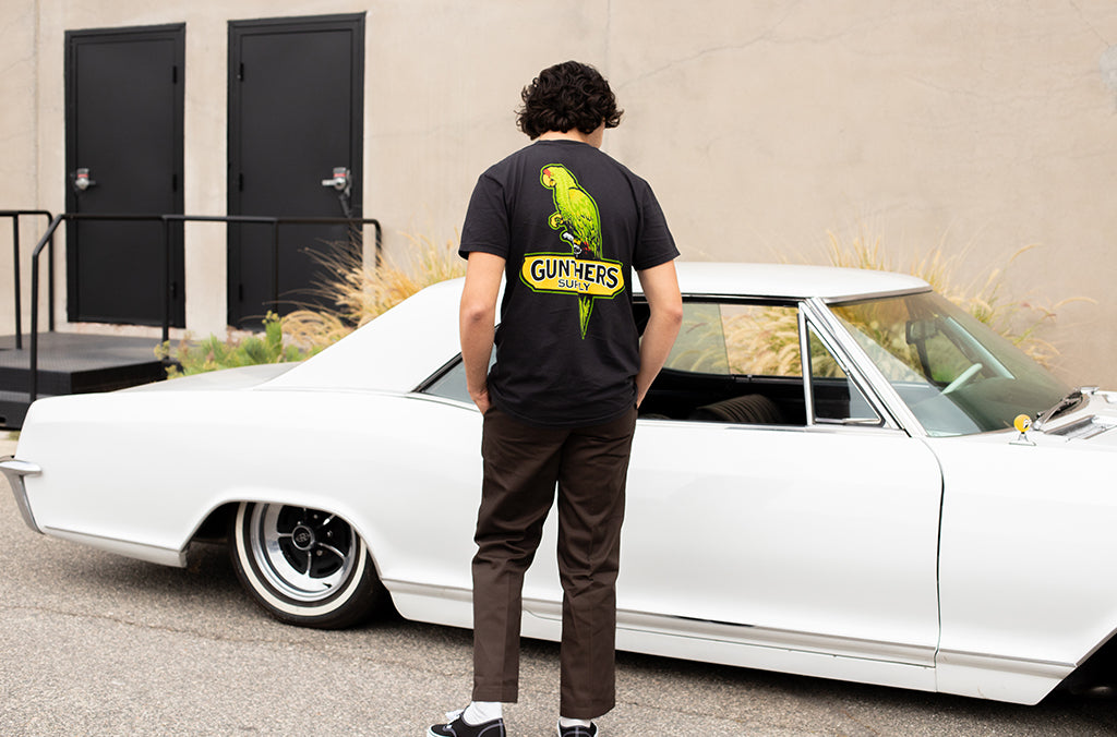 Person wearing a black t-shirt with a green parrot design, standing next to a white classic car.