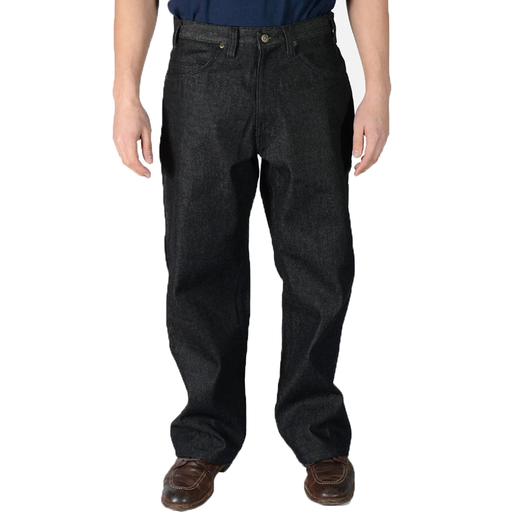 A person standing, wearing black denim carpenter pants with a button and zip fly closure, featuring front slash pockets, back patch pockets, and a hammer loop.