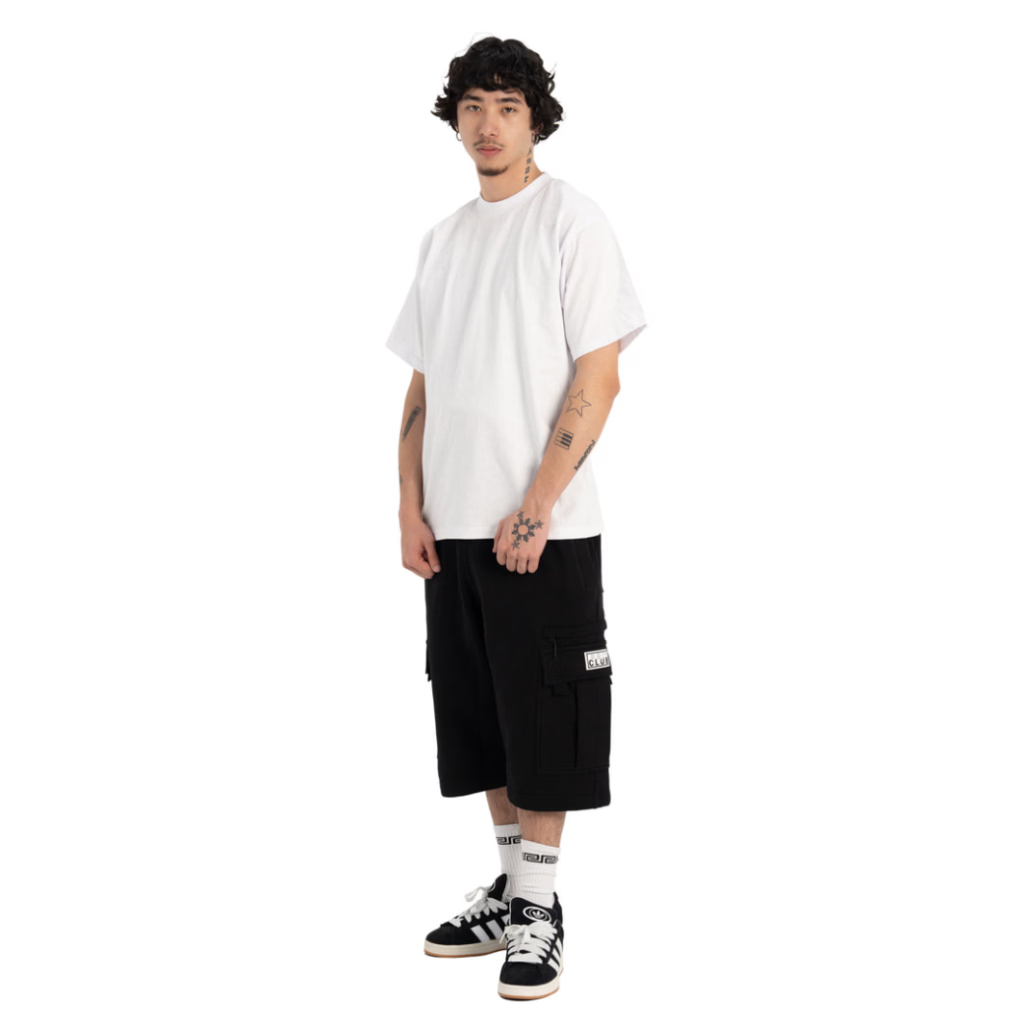 A model wearing a white crewneck t-shirt, black cargo shorts, white socks, and black and white sneakers, standing against a solid white background.