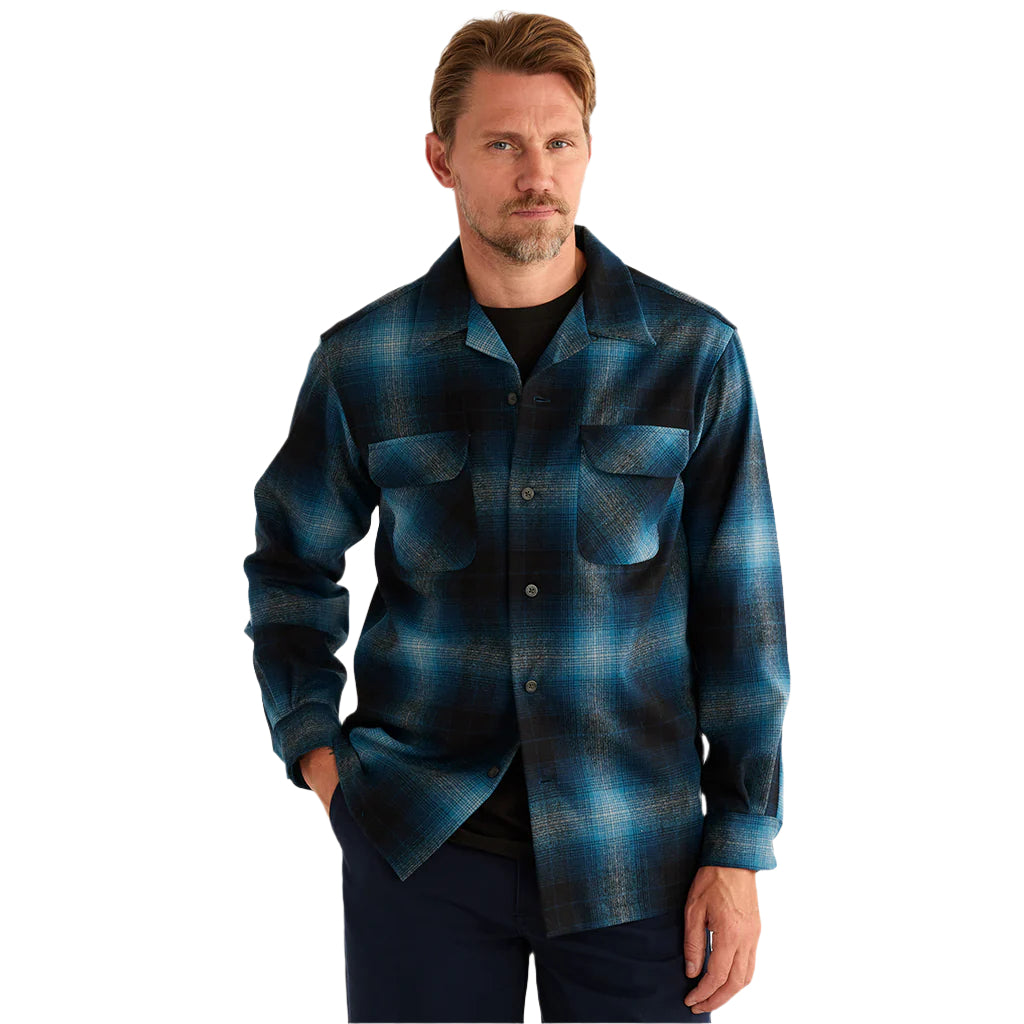 A male model wearing a long-sleeved, blue and black, checkered Pendleton shirt with two front pockets, standing against a neutral background.