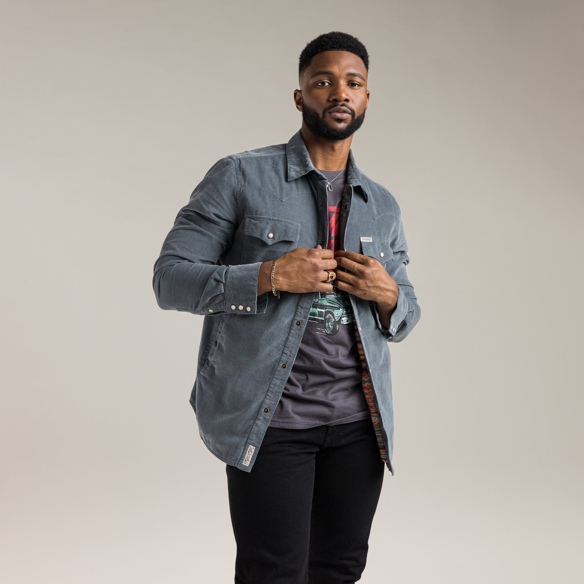 Man wearing a denim jacket over a plaid shirt on a plain background