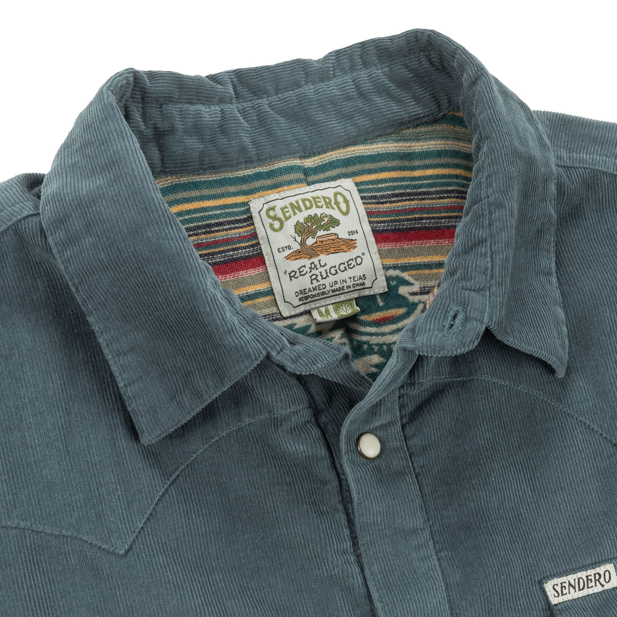 Close-up of a blue corduroy shirt with a Sendero label showing 'Real Rugged' text.
