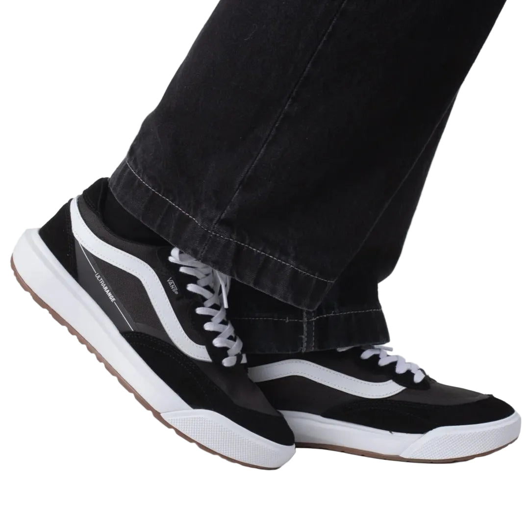 Black and white sneakers worn with black pants on a light gray background