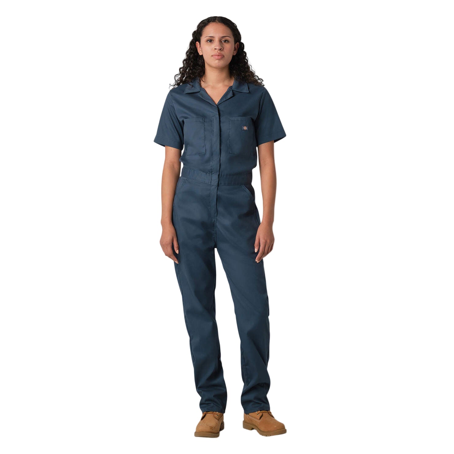 A woman standing, wearing short sleeve navy coveralls with a collar, two front pockets, and two hip pockets.