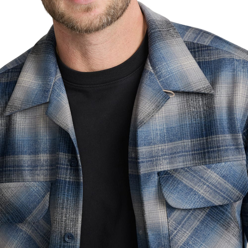 Man wearing a blue plaid shirt over a black t-shirt against a white background