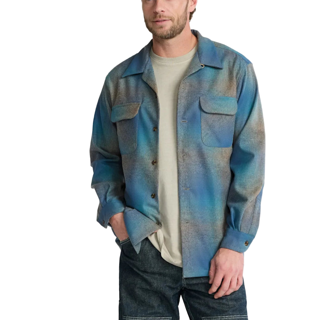 Man wearing a blue plaid shirt over a white t-shirt with a plain background