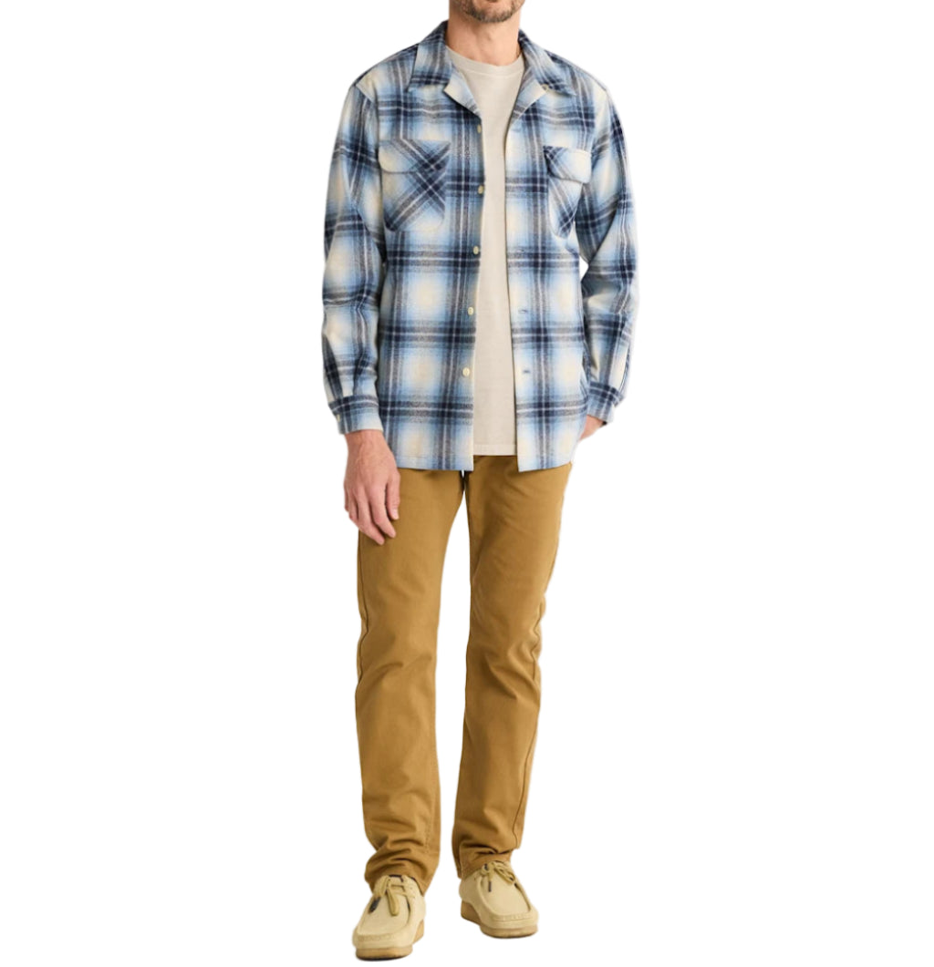 Man wearing a blue plaid shirt and tan pants on a white background