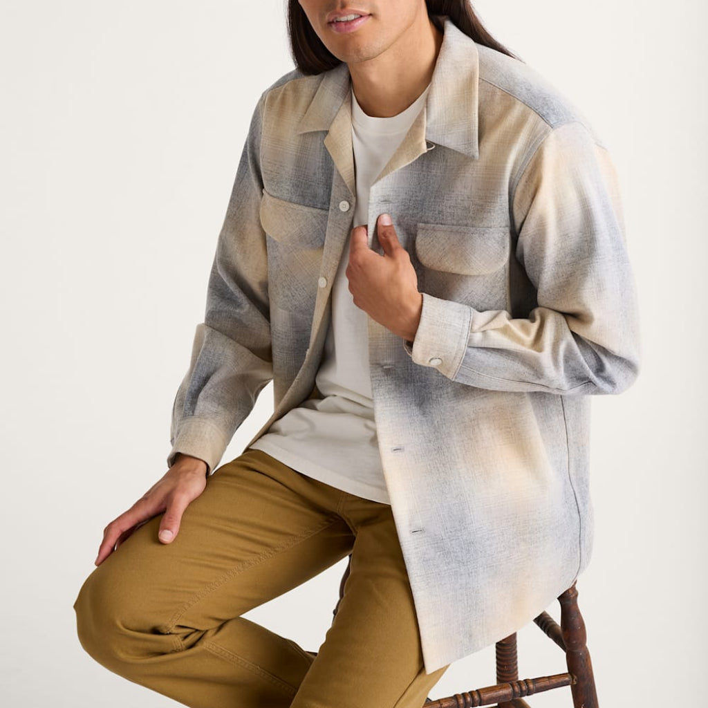 Person wearing a plaid shirt over a white t-shirt with brown pants on a white background