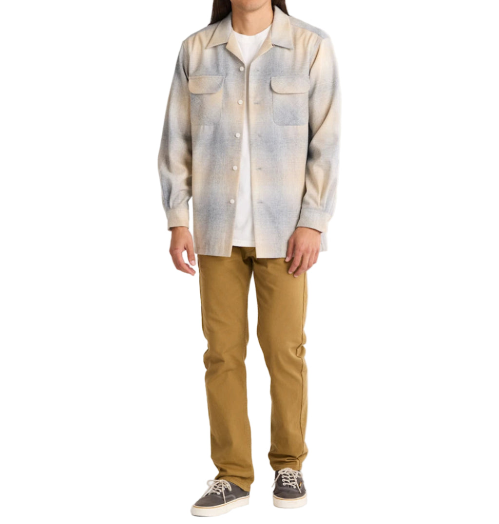 Man wearing a patterned shirt over a plain shirt with brown pants on a white background