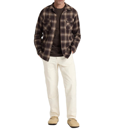 Man wearing a plaid shirt, dark sweater, white pants, and beige shoes on a white background