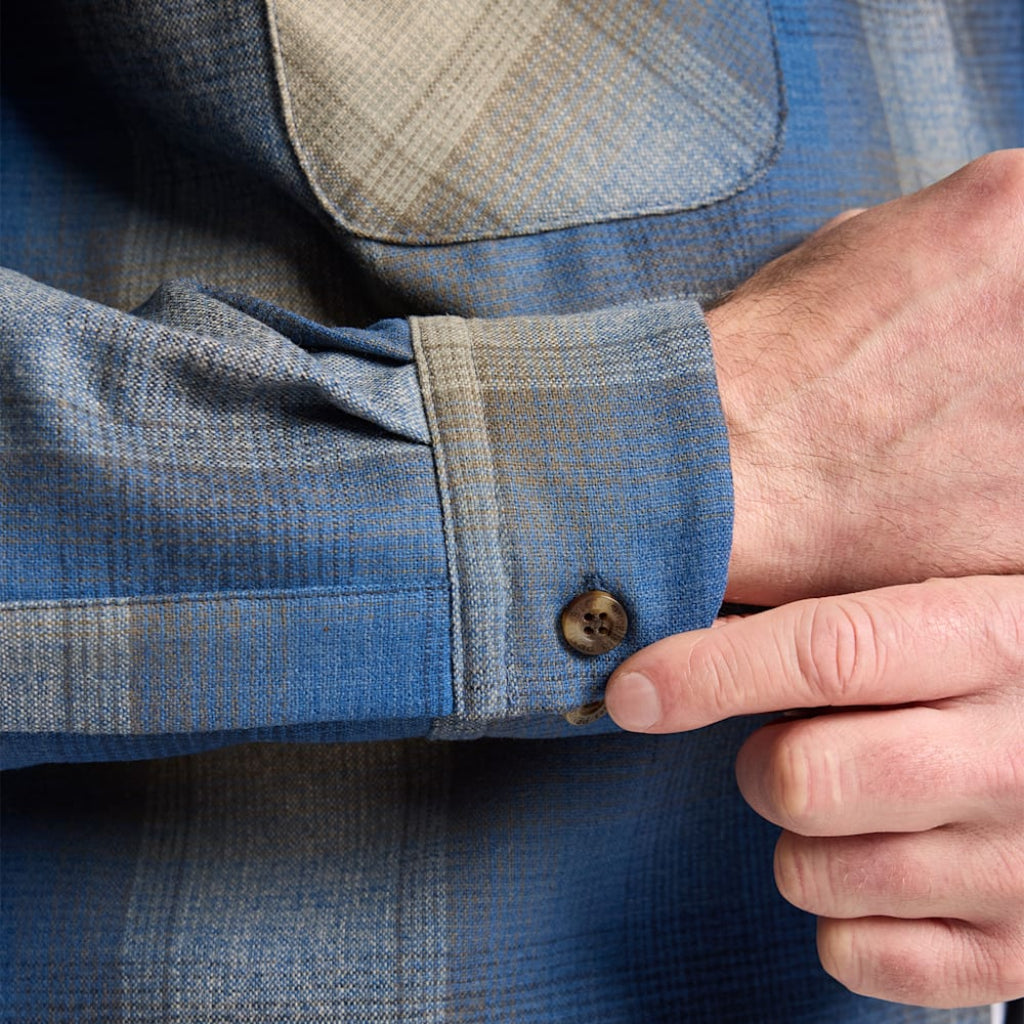 Close-up of a person adjusting the cuff of a blue plaid shirt.
