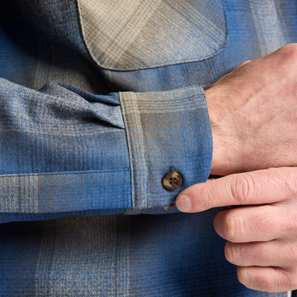 Close-up of a person adjusting the cuff of a blue plaid shirt.