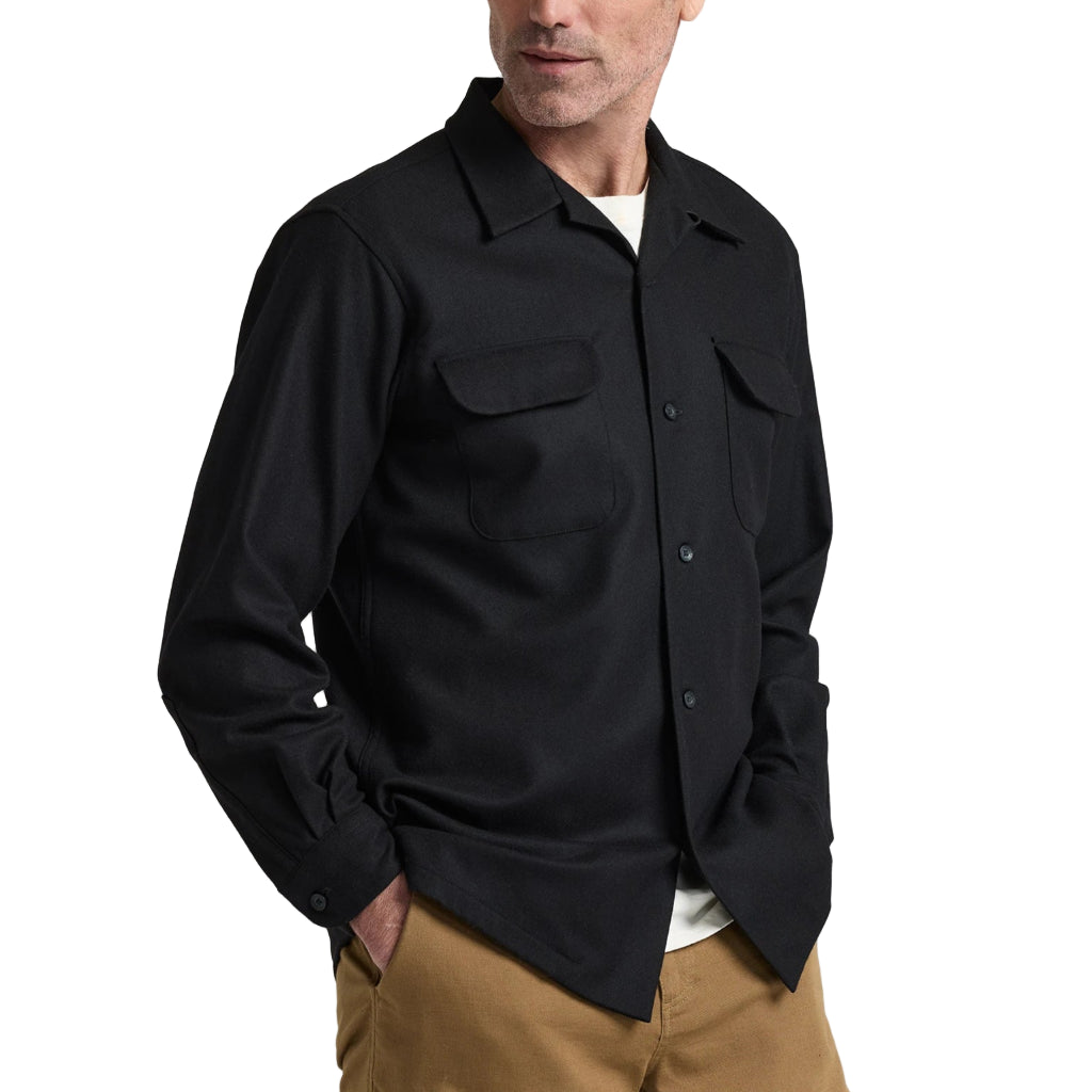Man wearing a black shirt and brown pants against a plain background