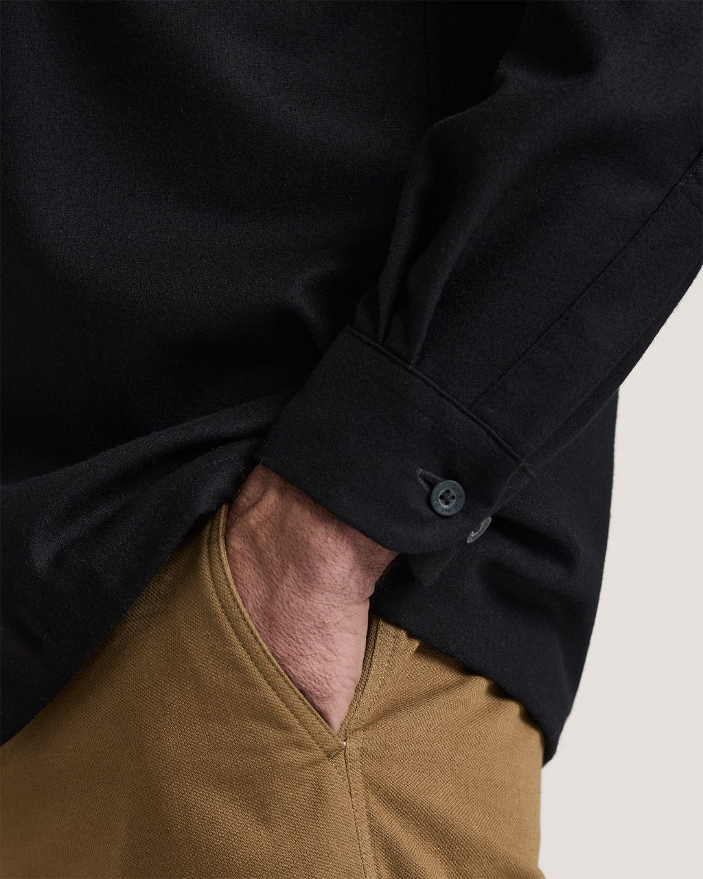 Close-up of a person wearing a black long-sleeve shirt and brown pants on a light background